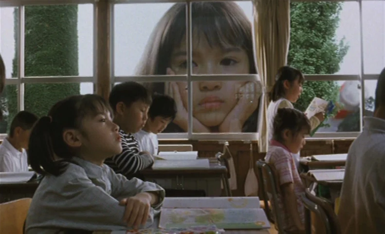 The Taste of Tea (2004) movie still: medium — A classroom interior features rows of students sitting at wooden desks near large windows. A giant…