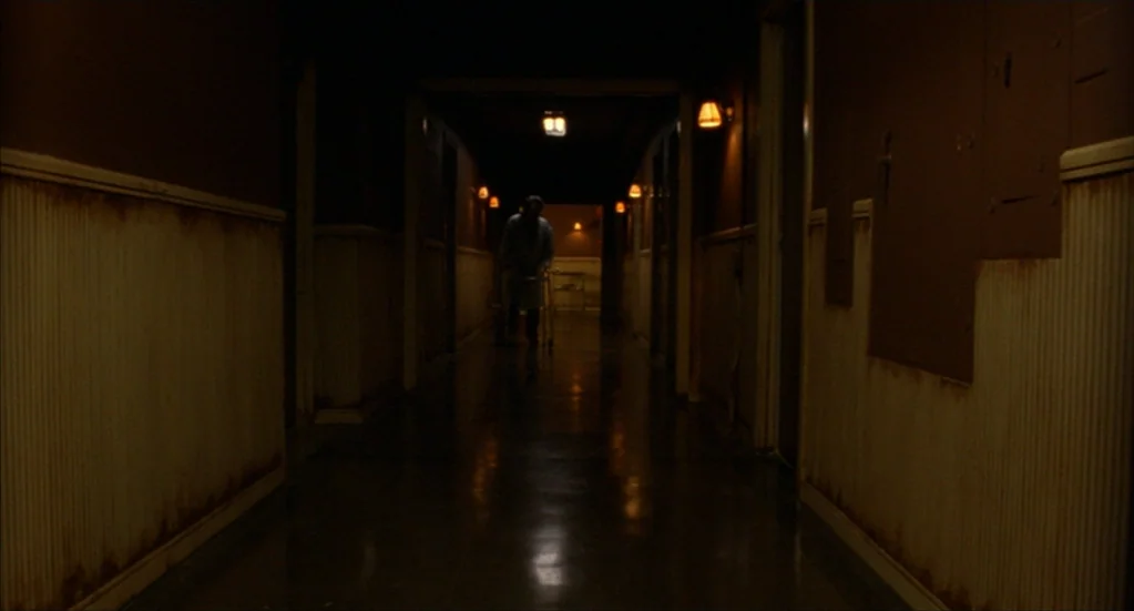Bubba Ho-Tep (2002) movie still: wide — A dark hospital hallway features scuffed walls with peeling beige wainscoting and polished floors. An…