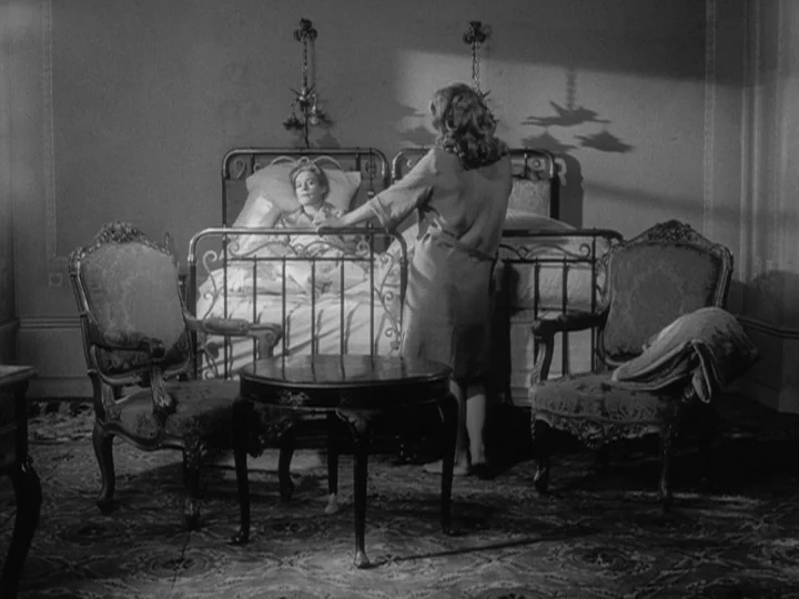 The Silence (1963) movie still: medium — A furnished interior featuring two ornate armchairs and a circular table in the foreground. One woman…