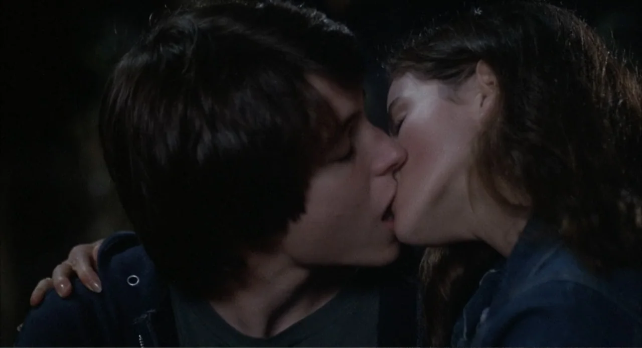 WarGames (1983) movie still: closeup — A dimly lit outdoor space at night with darkness surrounding the subjects. A young man and a young woman are…
