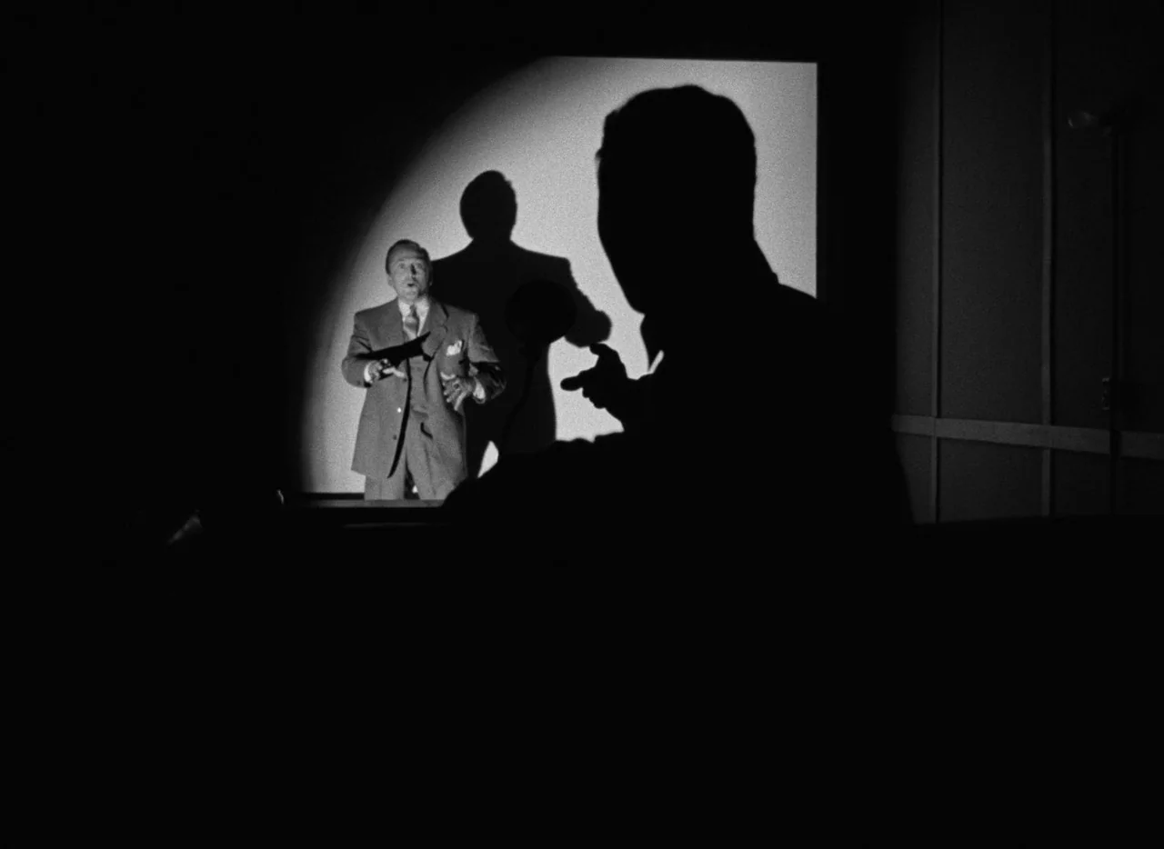 The Bad and the Beautiful (1952) movie still: medium — A man in a suit stands in the bright glow of a projection screen. A large dark silhouette of…