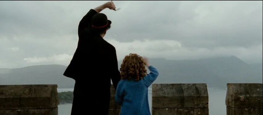 Mister Lonely (2007) movie still: fullbody — Stone crenelated ramparts overlook a body of water under a heavy grey sky. A man in a dark coat and a…