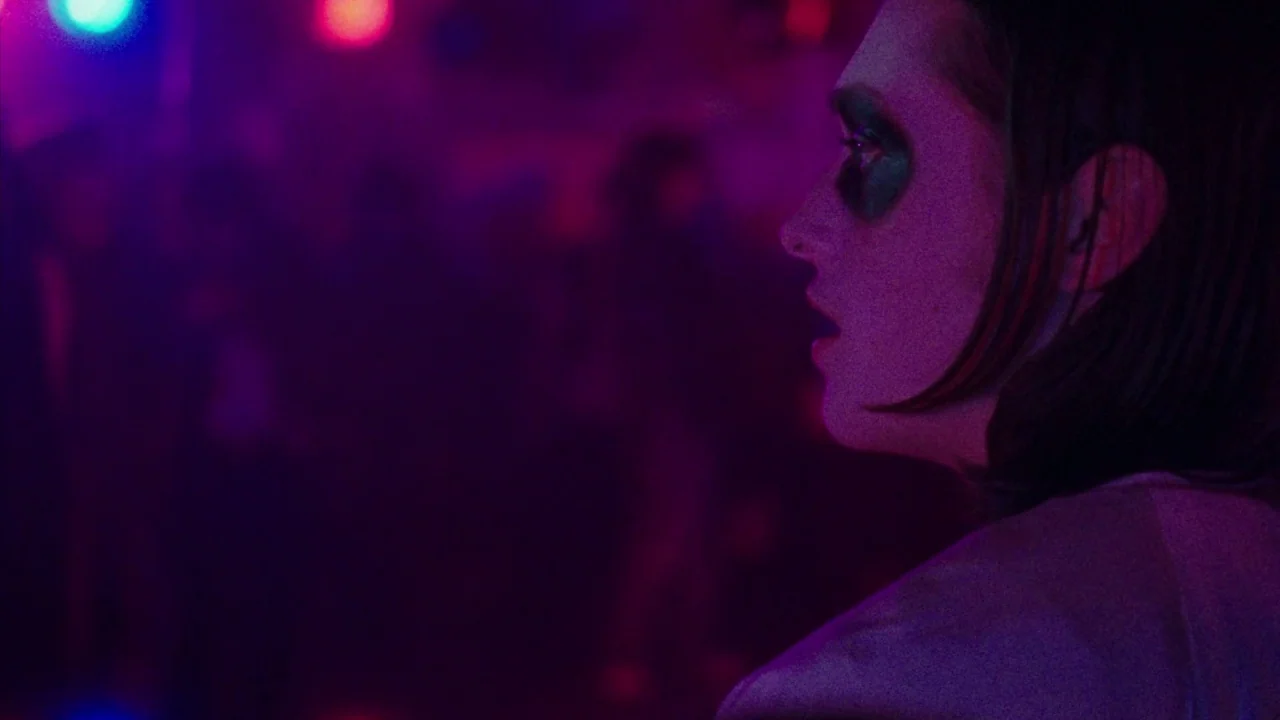 I Am Not a Serial Killer (2016) movie still: closeup — A dimly lit interior space features swirling vibrant purple and blue disco lights. A woman in…