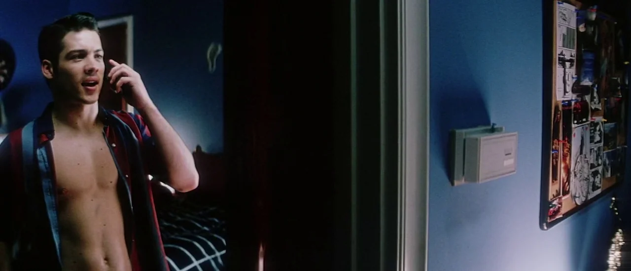 Pretty Persuasion (2005) movie still: medium — A dark hallway with blue-painted walls connects two adjacent rooms in a home. A young man stands…