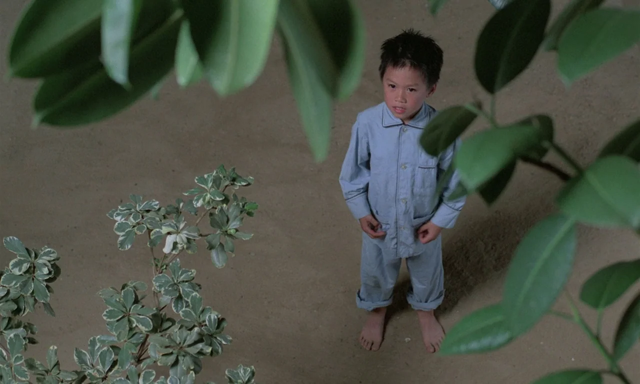 The Scent of Green Papaya (1993) movie still: fullbody — A sandy ground area is framed by lush green leaves in the immediate foreground. A young boy…