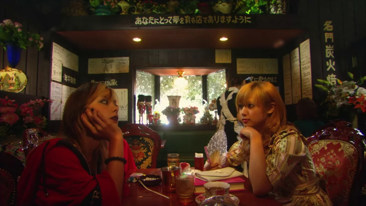Kamikaze Girls (2004) movie still: medium — An ornate, wood-paneled cafe features framed Japanese text and decor on the dark walls. Two young women…