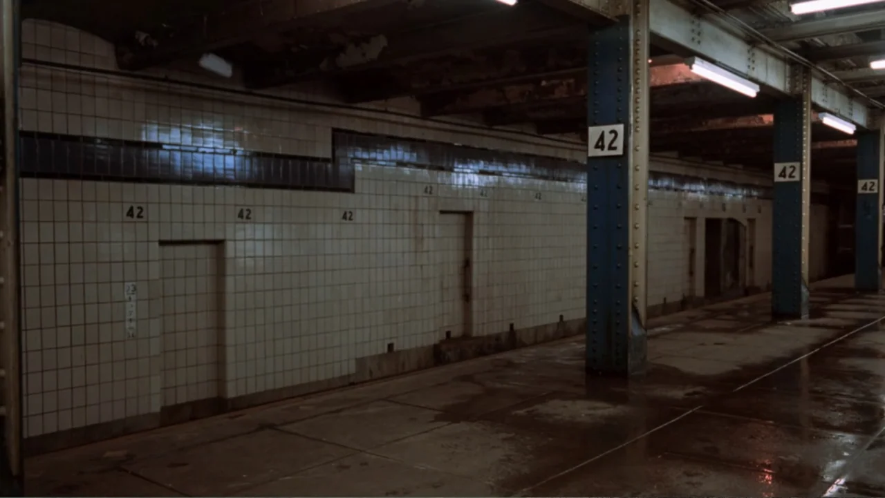 Ghost (1990) movie still: establishing — A dark subway platform featuring white tiled walls with repeating signs marked number 42. Rows of blue…