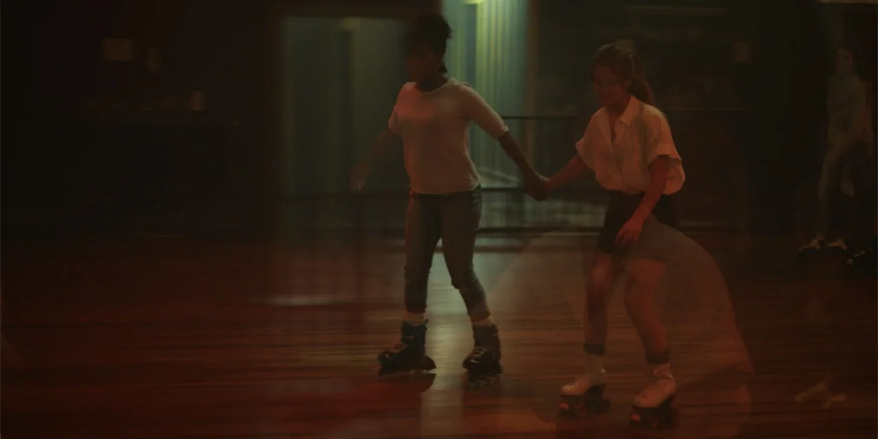La coda del diavolo (2024) movie still: fullbody — A dimly lit indoor roller rink with polished hardwood floors and dark surroundings. Two young…