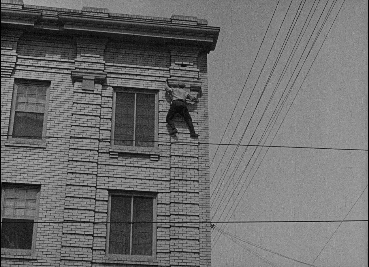 Safety Last! (1923) movie still: wide — A multi-story building facade made of light-colored bricks features large windows and grid masonry. A man in…
