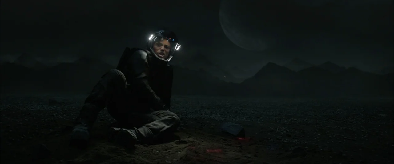 DISTANT (2026) movie still: fullbody — A barren dark alien landscape with rocky terrain and a large moon in sight. An astronaut sits on the dirt…