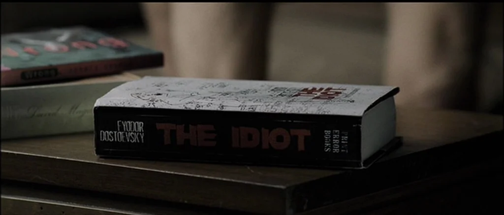 The Machinist (2004) movie still: closeup — A close up of a paperback copy of The Idiot by Fyodor Dostoevsky. The book rests on a dark wooden…