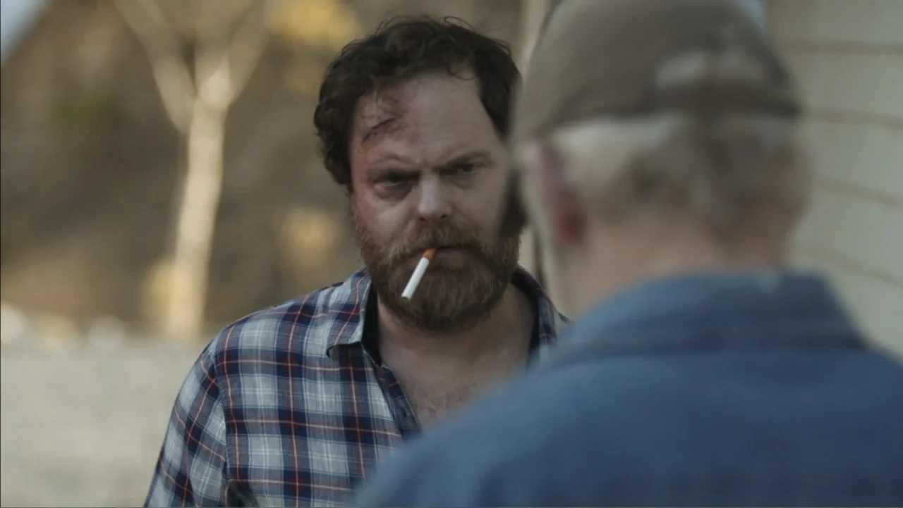 Boy (2010) movie still: medium — A rural setting with a blurred background of trees and gravel ground. Two men engage in conversation while standing…