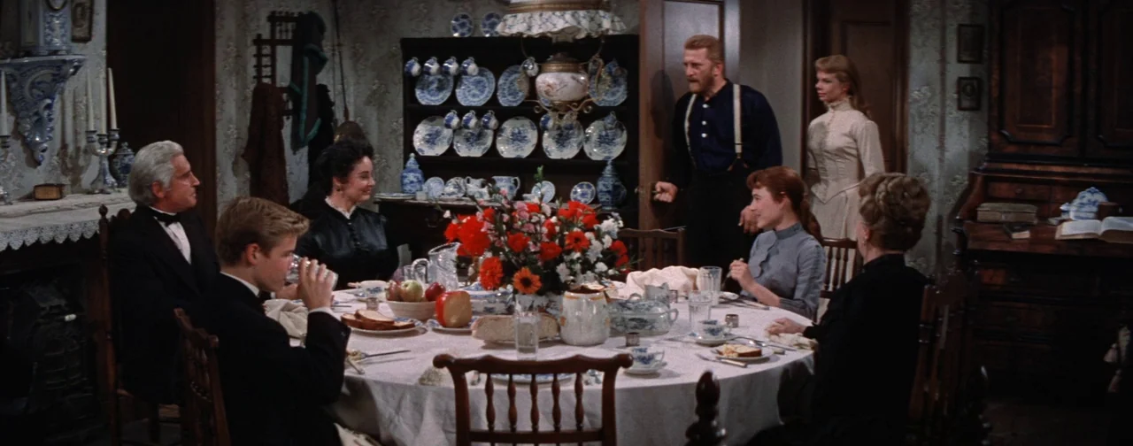 Lust For Life (1956) movie still: wide — A turn-of-the-century dining room features wallpaper with floral patterns and a china cabinet. Six people…