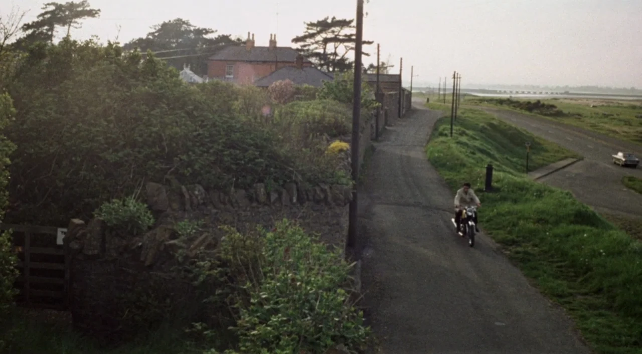 The Iguana with the Tongue of Fire (1971) movie still: wide — A quiet rural landscape features a narrow asphalt road bordered by stone walls. A lone…