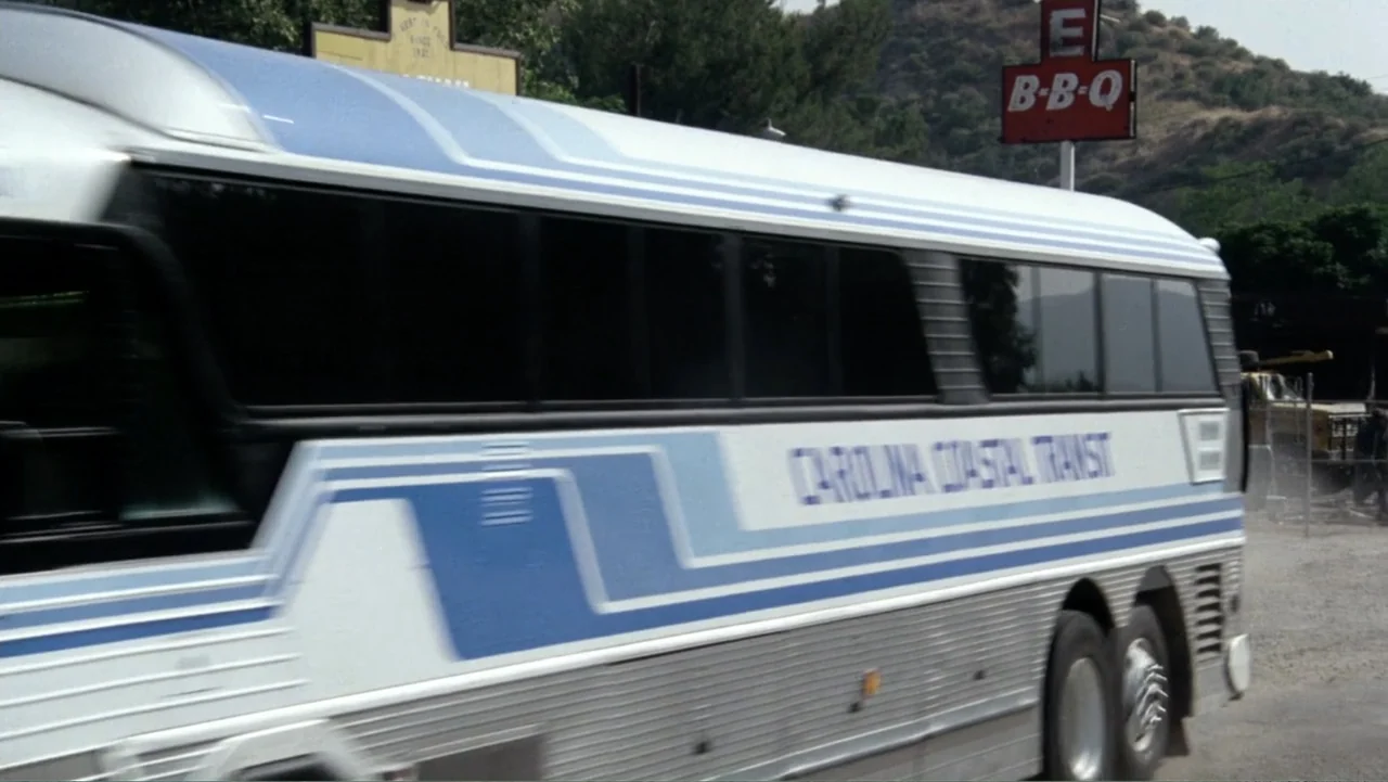 Heartbreak Ridge (1986) movie still: medium — A passenger bus drives past a roadside barbecue restaurant on a sunny day. The large white and blue…