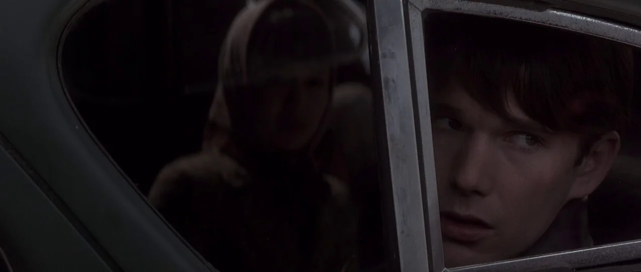 Snow Falling on Cedars (1999) movie still: closeup — A dark car interior at night with a man in the foreground and a woman in the background. The…