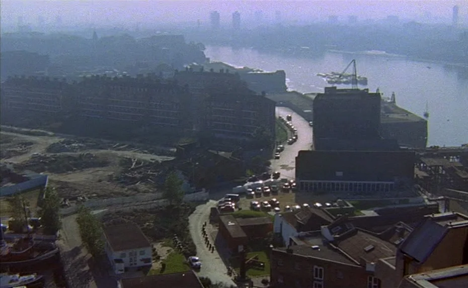 To The Devil a Daughter (1976) movie still: establishing — An aerial view captures a sprawling, partially industrial dockside area during the…