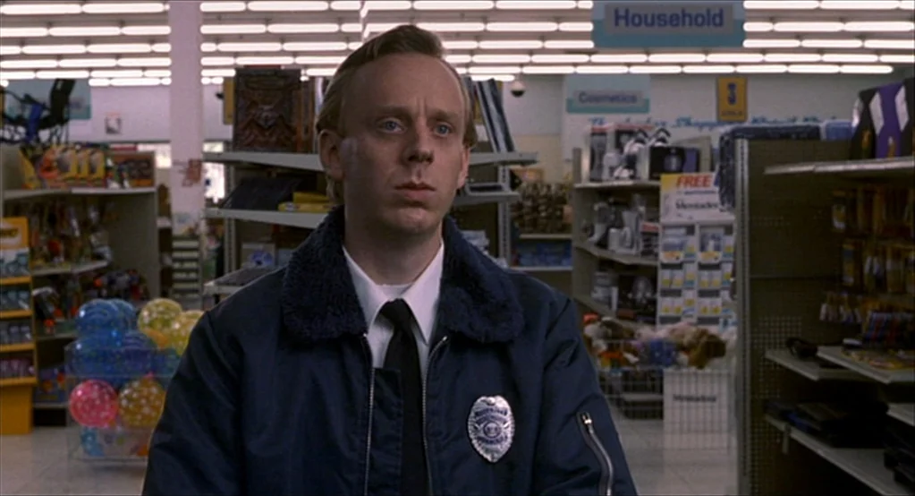 The Good Girl (2002) movie still: medium — The interior of a brightly lit retail store with shelves stocked with various products. A man wearing a…