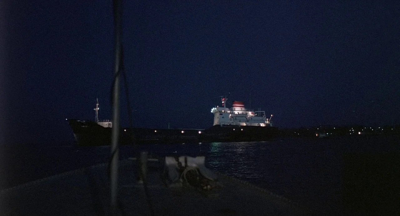 Ariel (1988) movie still: wide — A dark cargo ship illuminated by navigation lights travels across a nighttime sea. The view is from another vessel…