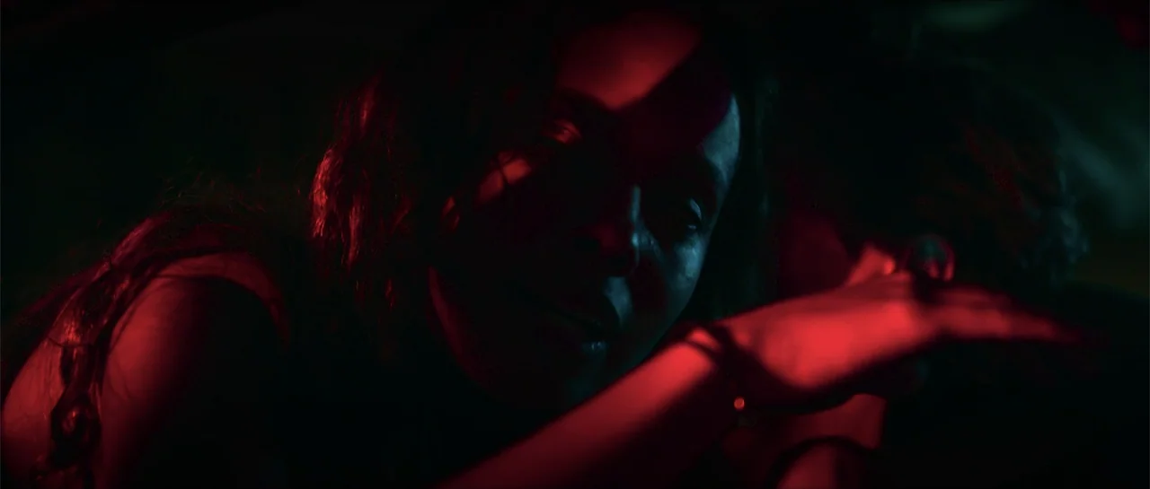 68 Kill (2017) movie still: closeup — A dimly lit car interior is bathed in deep red and green light. A woman is seen in closeup with her arm…