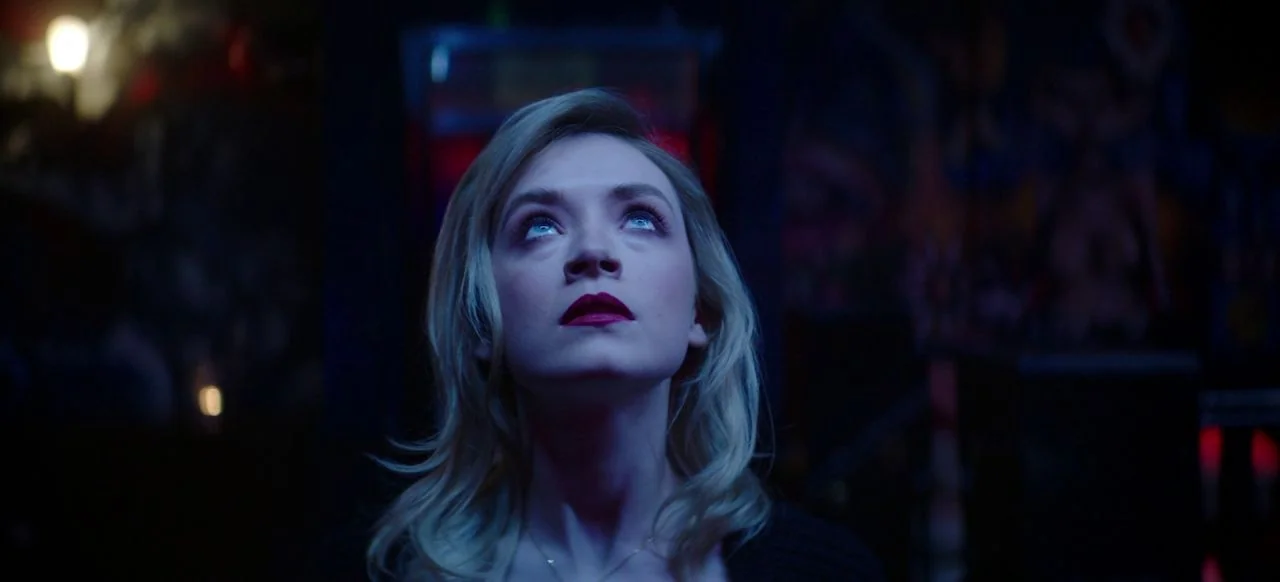 A Good Woman Is Hard To Find (2019) movie still: closeup — A dark space lit by neon lights with indistinct shapes in the background. A young woman…