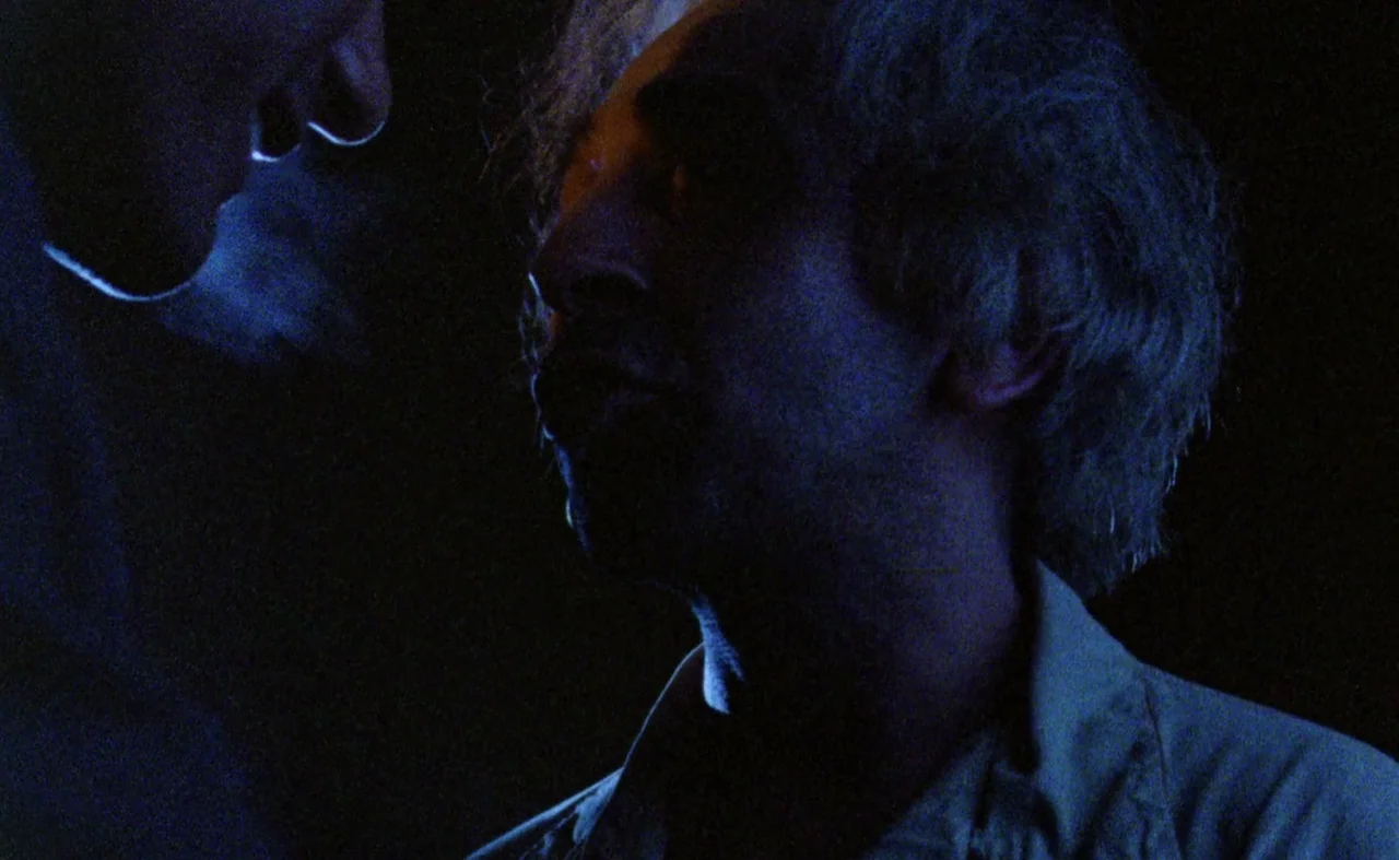 My Beautiful Laundrette (1985) movie still: closeup — A dark, dimly lit interior space with shadows obscuring most architectural details. An older…