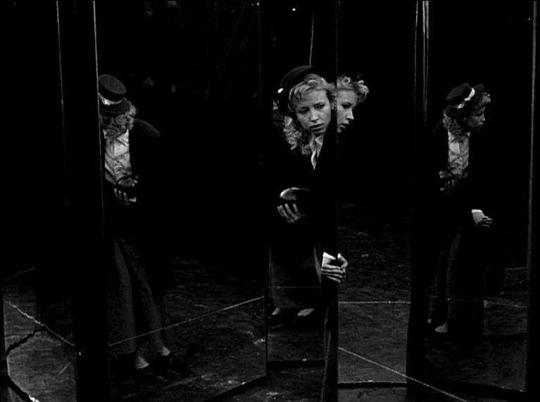 My 20th Century (1989) movie still: medium — A woman stands within a series of vertical mirrors in a dark setting. She looks through a gap between…