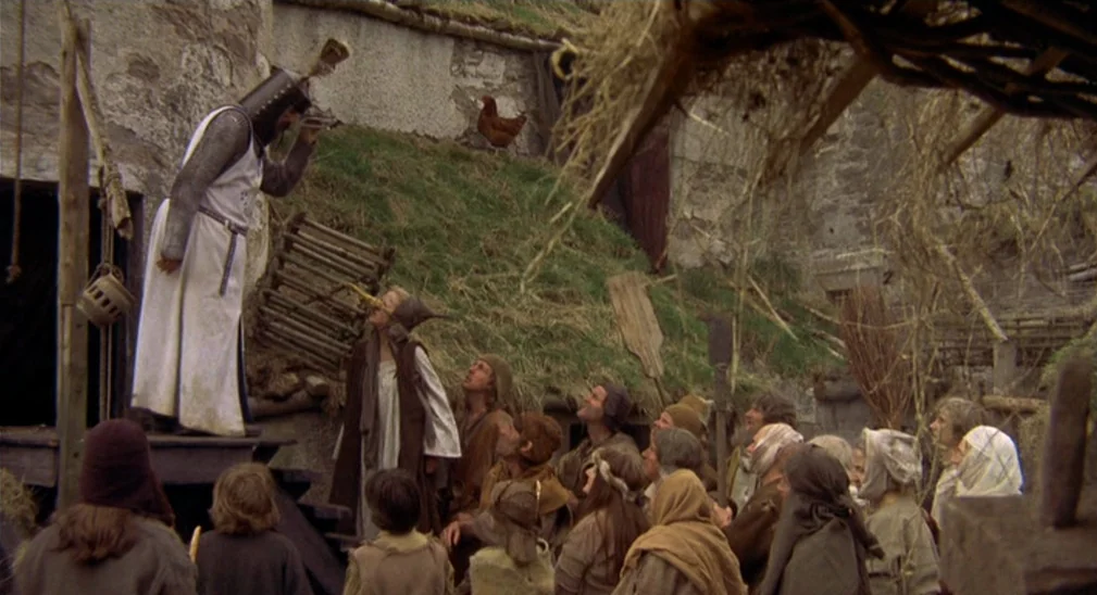 Monty Python and the Holy Grail (1975) movie still: wide — A rural settlement features stone huts with earth-covered, grassy roofs and wooden…