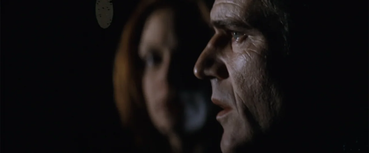 Conspiracy Theory (1997) movie still: closeup — A dark, dimly lit interior space with shadows obscuring most architectural details. A man in profile…