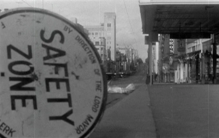 On The Beach (1959) movie still: wide — An urban city street is viewed with a large, blurred safety zone sign in foreground. The street appears…