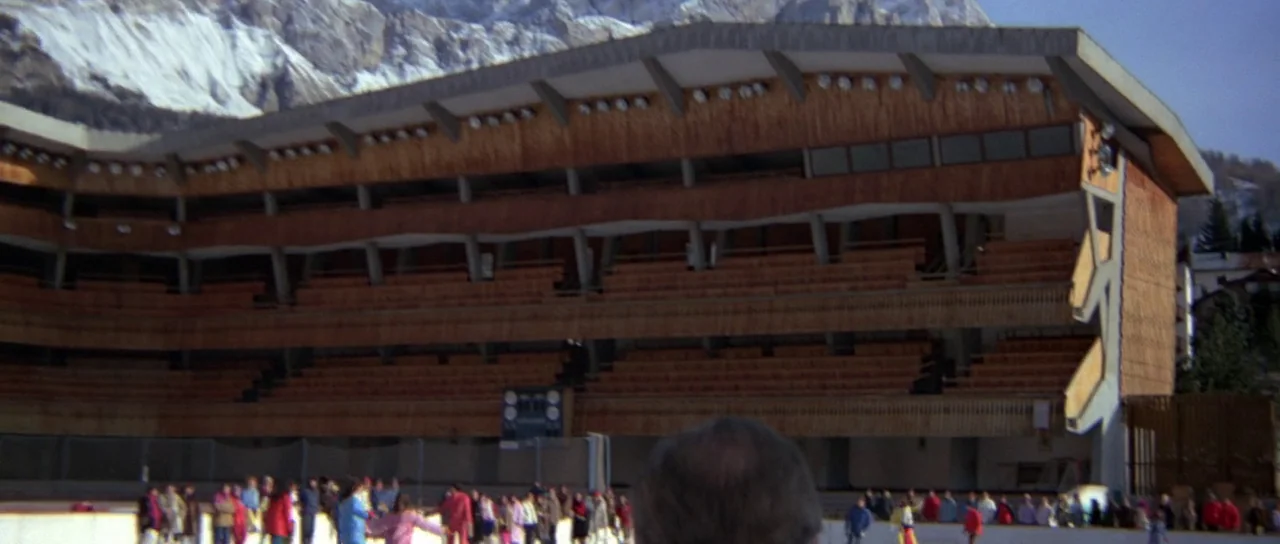 For Your Eyes Only (1981) movie still: wide — A modern outdoor ice rink features tiered wooden grandstands backed by snow-covered mountain peaks. A…