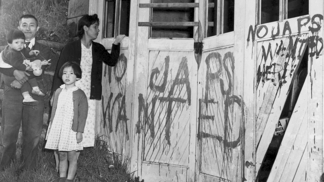 The Soul of America (2020) movie still: medium — An East Asian family stands before a large wooden door marked with offensive graffiti. The graffiti…