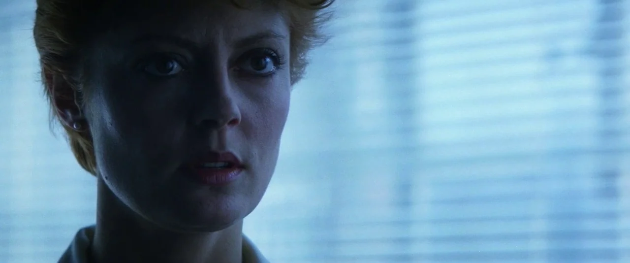 The Hunger (1983) movie still: closeup — An interior space features horizontal window blinds filtering daylight into the room. A woman looks forward…
