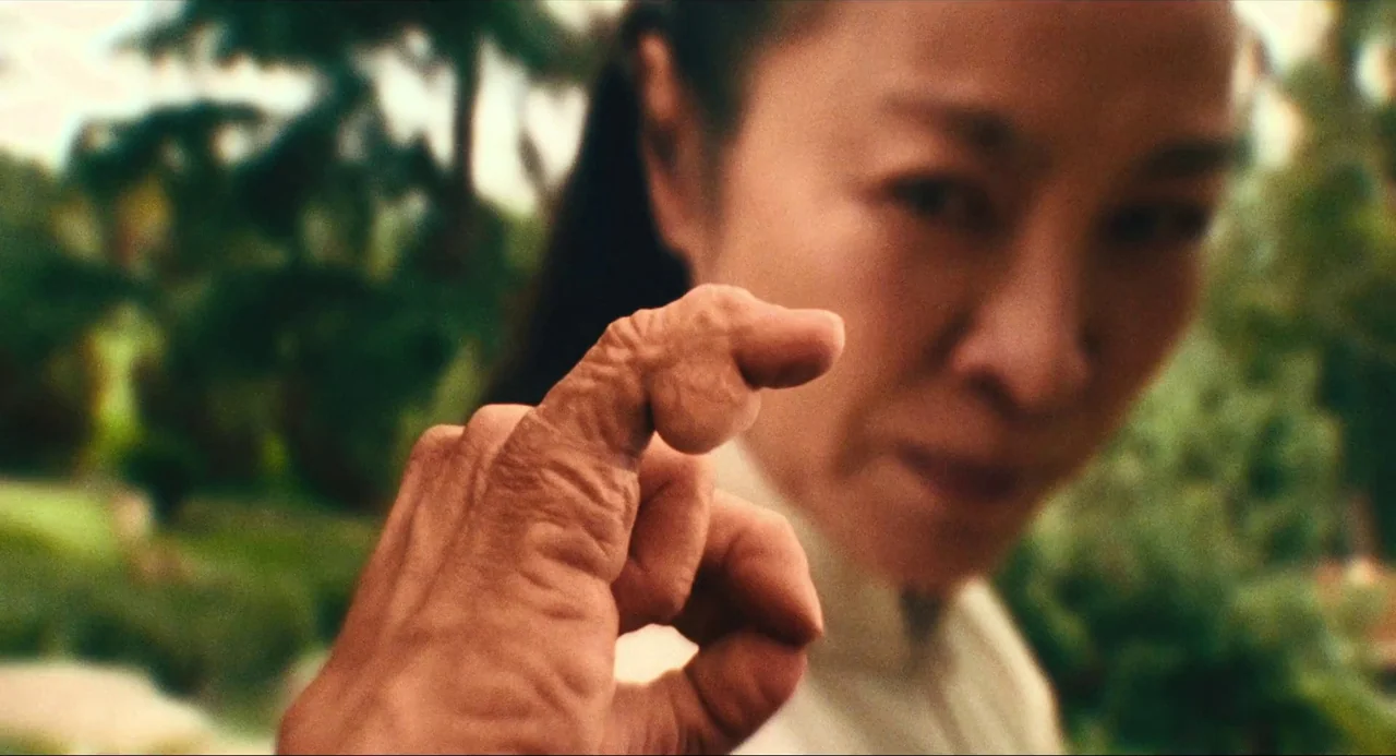 Everything Everywhere All At Once (2022) movie still: closeup — A woman stares directly into the lens while extending a hand toward the camera. Her…