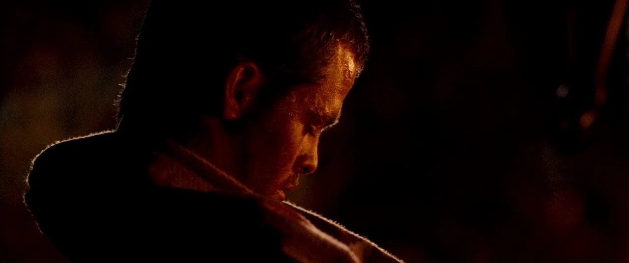 Carriers (2009) movie still: closeup — A dark, underexposed interior space features deep shadows obscuring the surrounding environment. A man's side…