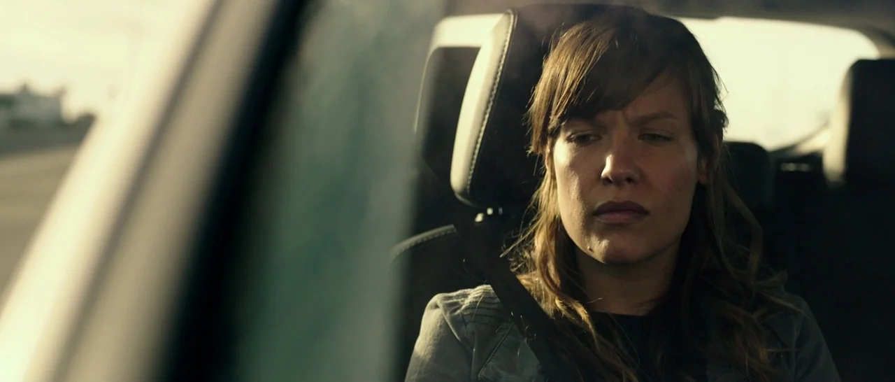 The Purge: Anarchy (2014) movie still: closeup — The interior of a moving car shows a woman sitting in the passenger seat. She is looking forward…