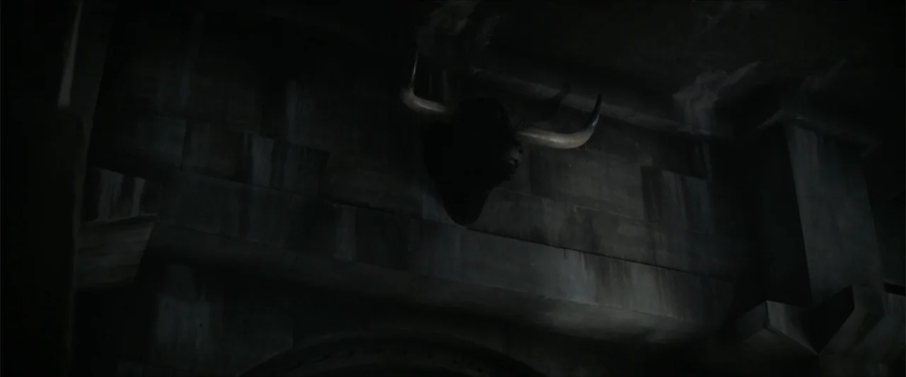 Dune (2021) movie still: medium — A dark stone wall features a large bull head trophy mounted centrally. The surface is composed of large, weathered…