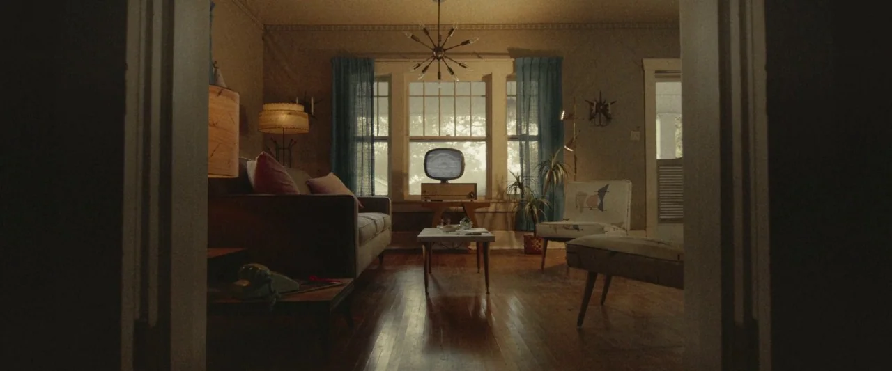 The Vast of Night (2019) movie still: wide — A 1950s style room features mid-century modern furniture, a vintage television, and blue curtains. The…