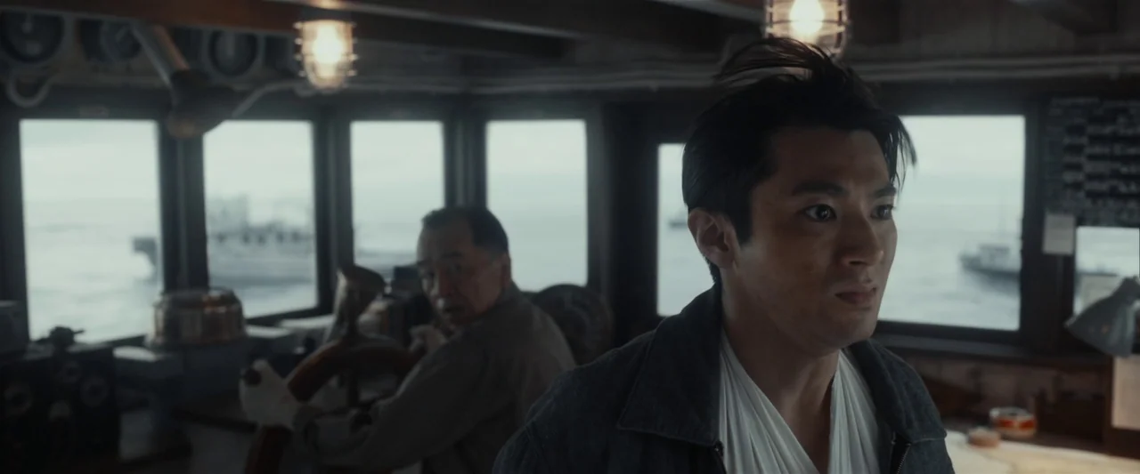 Godzilla Minus One (2023) movie still: medium — The interior of a mid-century vessel bridge features glass windows looking out at sea. A young man…