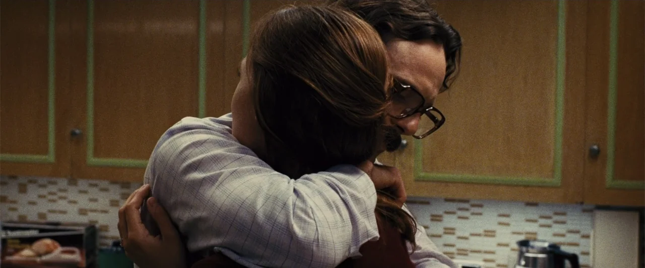 Argo (2012) movie still: medium — A 1970s kitchen with wood-finish cabinets and a tiled backsplash is visible. A man and a woman are hugging each…