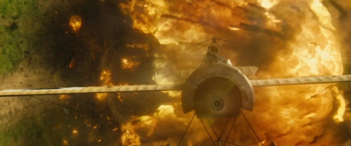 Wonder Woman (2017) movie still: wide — A single-engine propeller plane flies directly away from a massive fiery explosion. Large billows of orange…