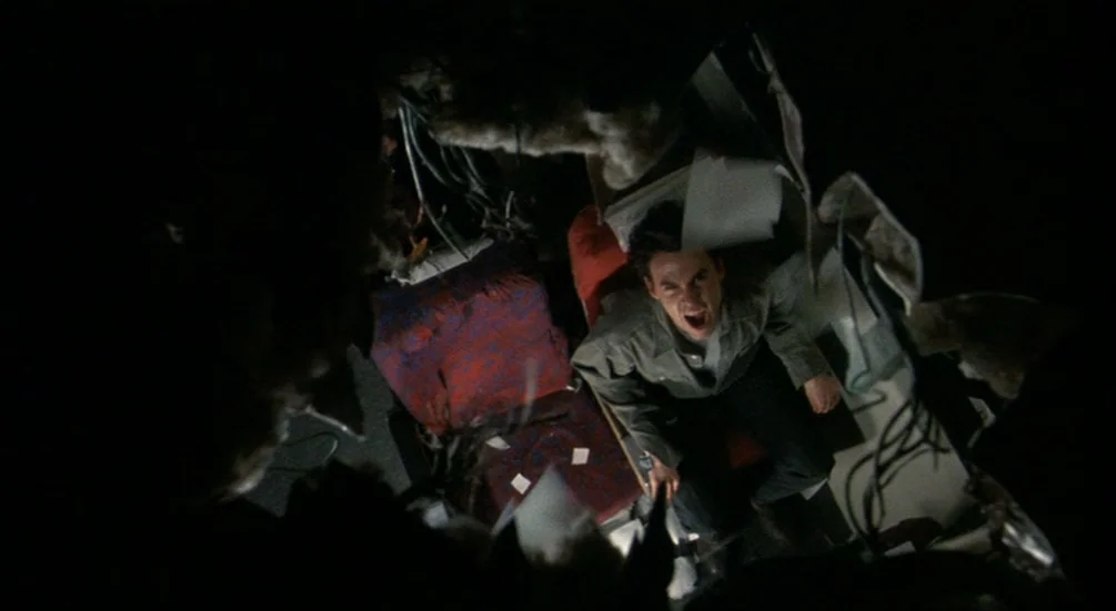 Freddy’s Dead: The Final Nightmare (1991) movie still: medium — A man sits inside a dark and cramped space surrounded by debris and wires. The man…