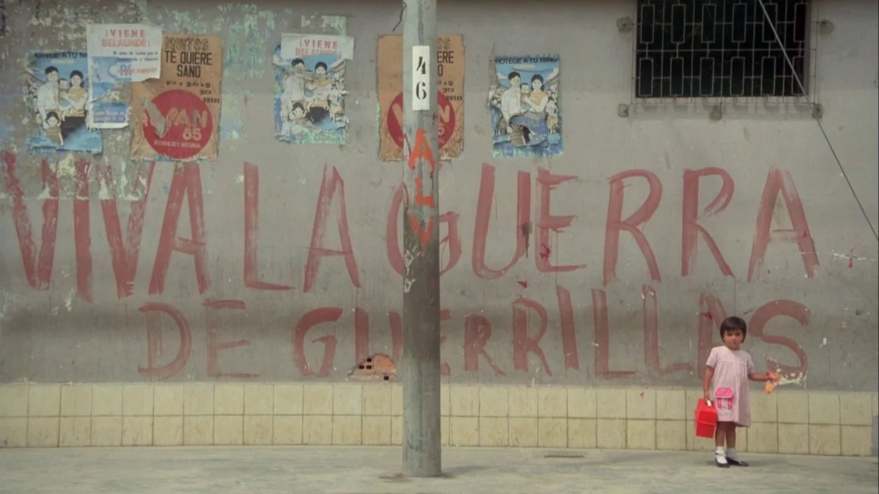 Powaqqatsi (1988) movie still: wide — A weathered concrete wall is covered with red propaganda graffiti and multiple paper posters. A lone young…