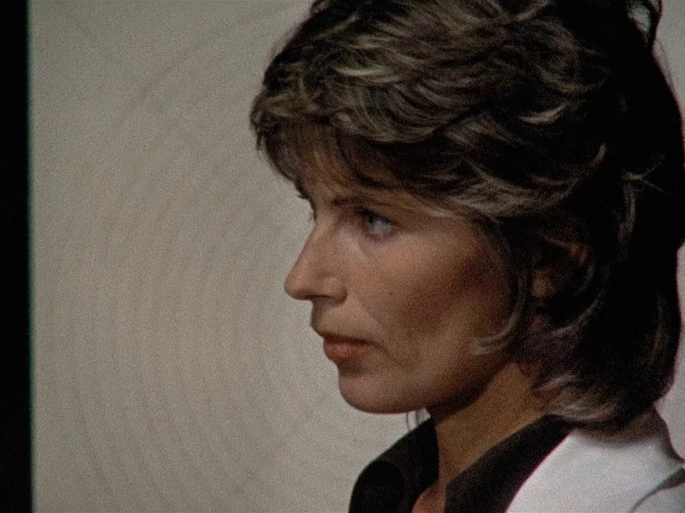Scenes from a Marriage (1973) movie still: closeup — A woman stands in a plain room with light-colored walls behind her. She looks off-screen while…
