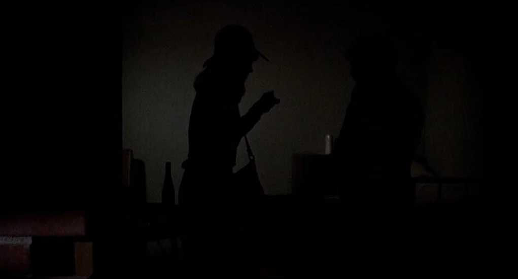 Family Plot (1976) movie still: medium — A dimly lit room features two silhouetted figures facing each other in the darkness. One person wears a…