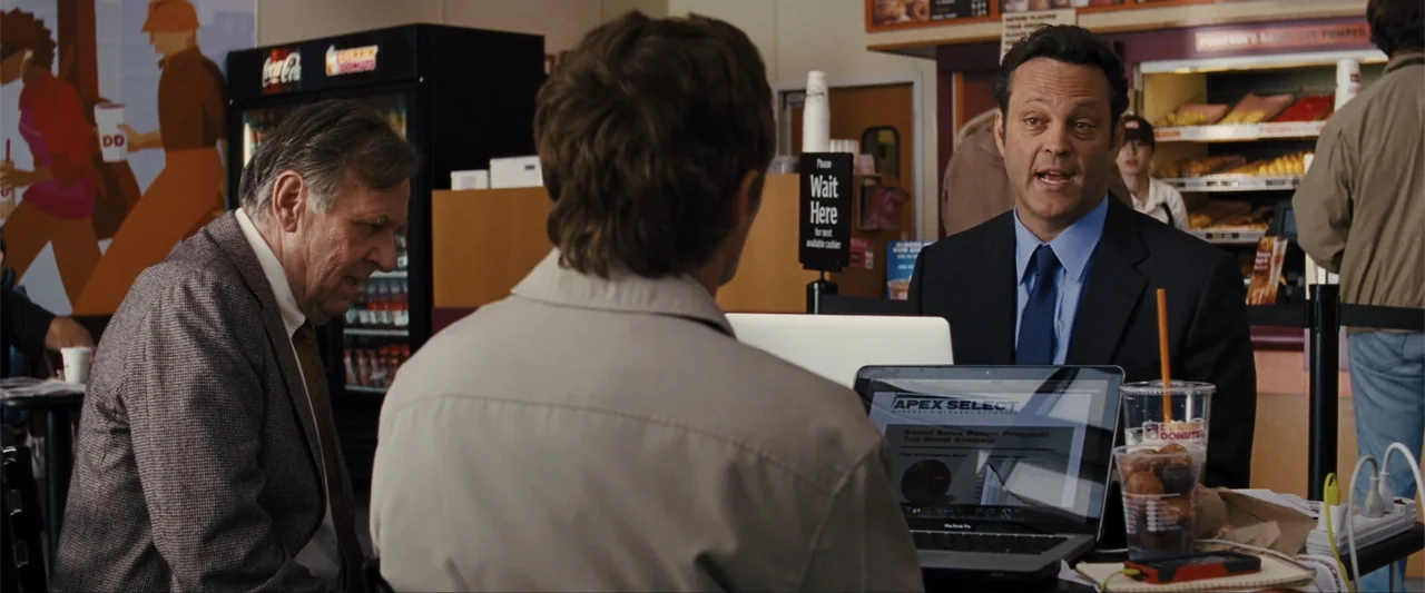 Unfinished Business (2015) movie still: medium — A bright restaurant interior features a table with a laptop and donut containers. A man in a suit…