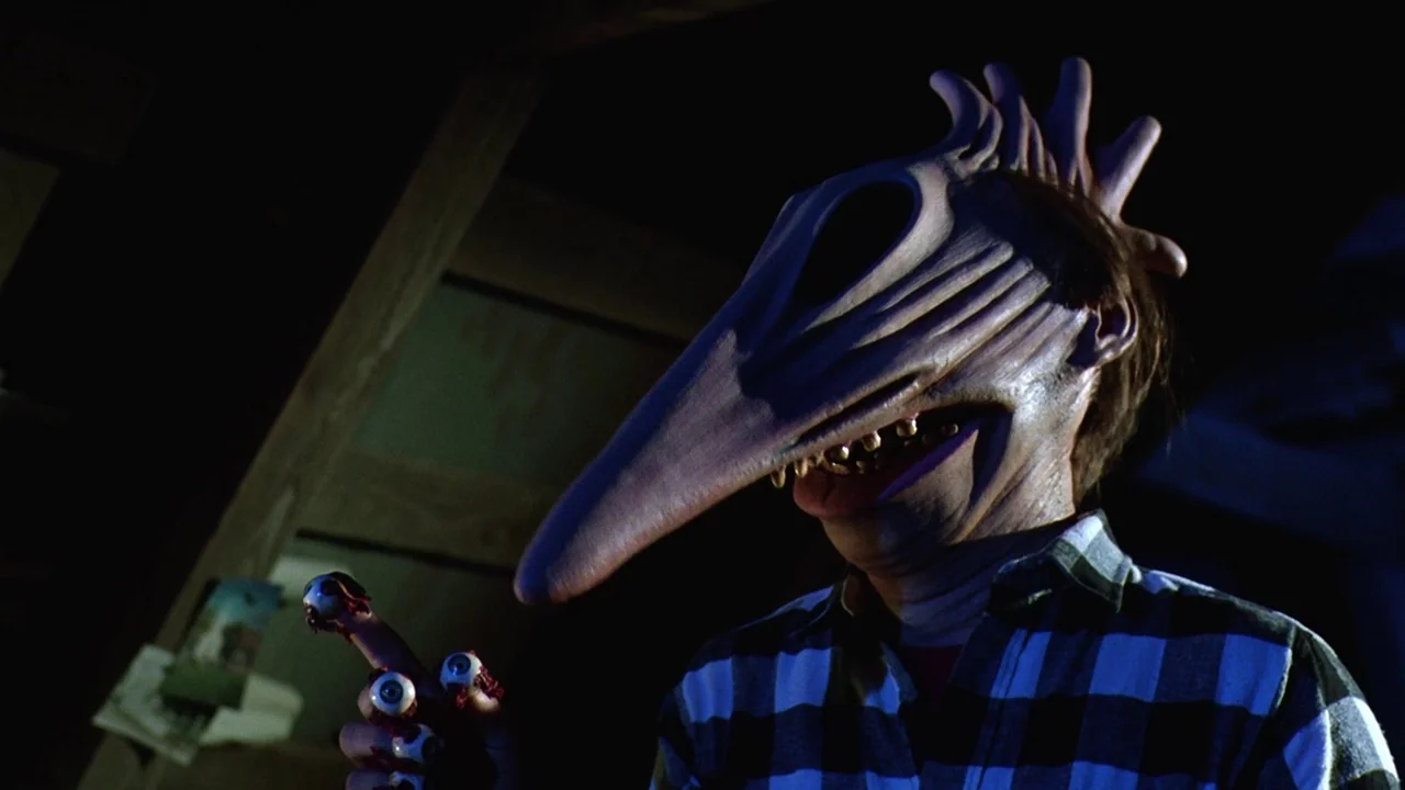 Beetlejuice (1988) movie still: medium — A dark, cramped attic space features wooden rafters visible in the shadowed background. A figure wearing an…
