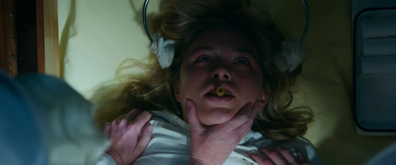 Don’t Worry Darling (2022) movie still: closeup — A sterile medical room features a pale yellow surface and clinical equipment. A woman lying on her…