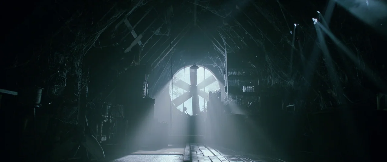 Malignant (2021) movie still: establishing — A dark, cluttered space is filled with heavy cobwebs and wooden rafters. A single circular industrial…
