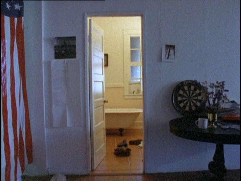 Totally F***ed Up (1993) movie still: wide — An interior shot shows a dimly lit living space transitioning into a bright bathroom. A large American…